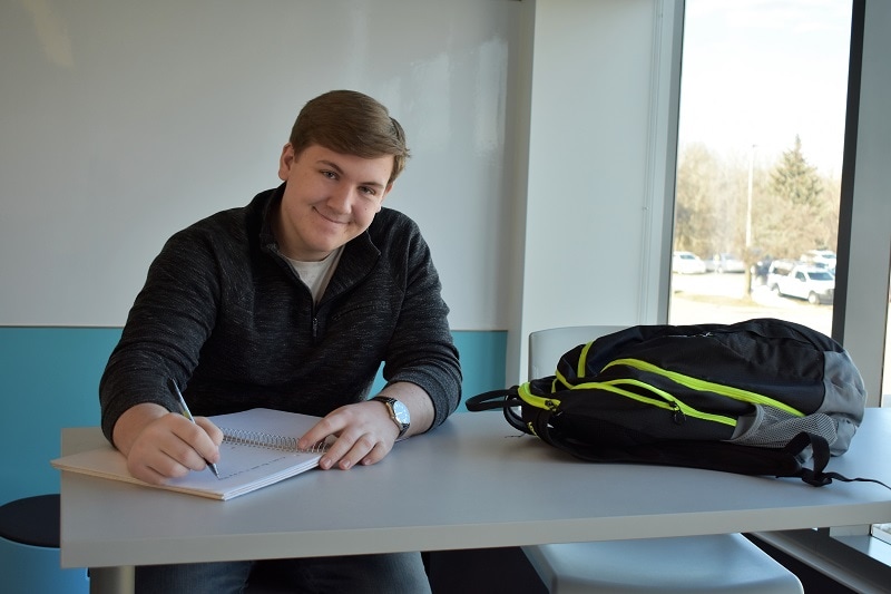 male student sitting at desk writing in a notebook