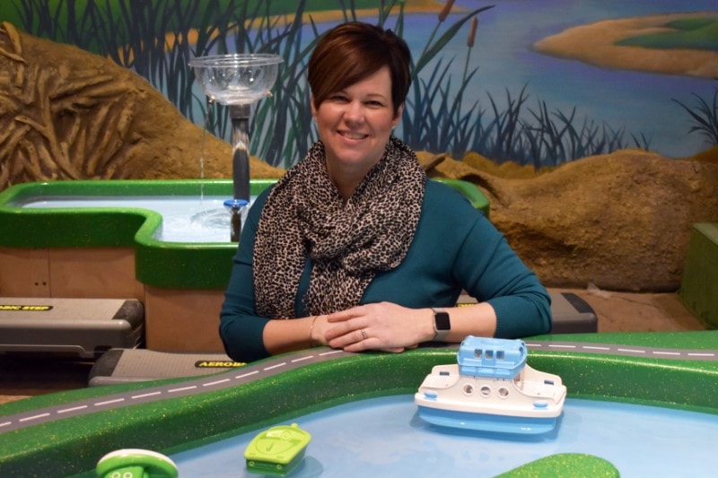 woman leans on a water play table with floating boats in front of her