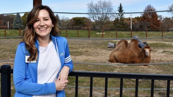 woman leaning against a railing with a camel in the background