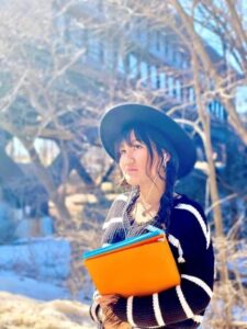 student wearing hat holding binders standing outdoors