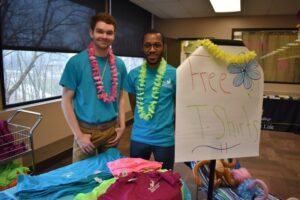 two students standing next to sign that says "free t-shirts" and a table covered with t-shirts