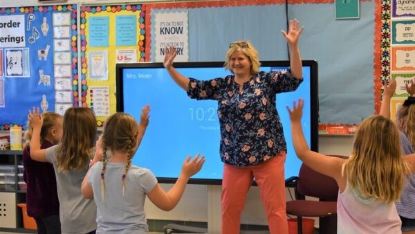 music teacher and students holding their arms up while moving to the beat of a song