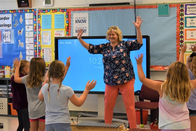 music teacher and students holding their arms up while moving to the beat of a song