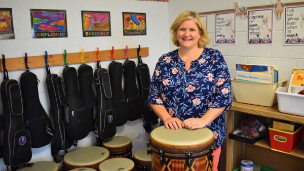 music teacher behind a drum with drums and ukuleles behind her