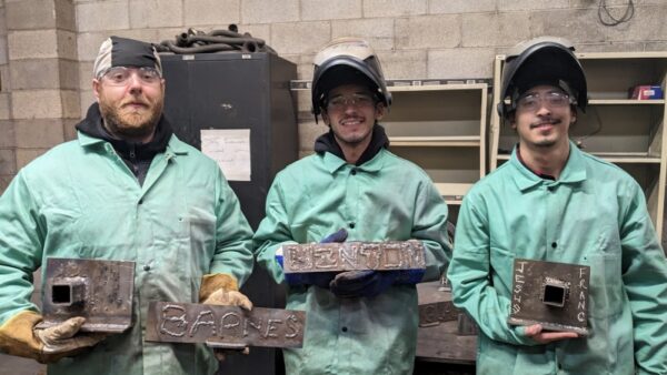 3 students in welding gear holding up nameplates they welded