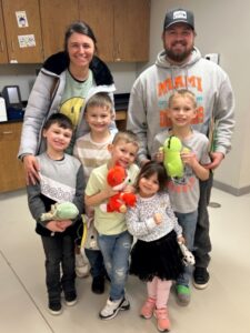 5 kids with stuffed animals and 2 adults smiling at camera