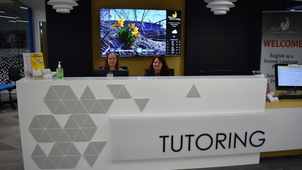 two employees sitting at a large white desk that says Tutoring