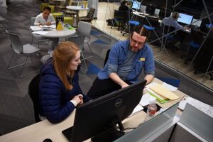 student and tutor talk while sitting at a computer station