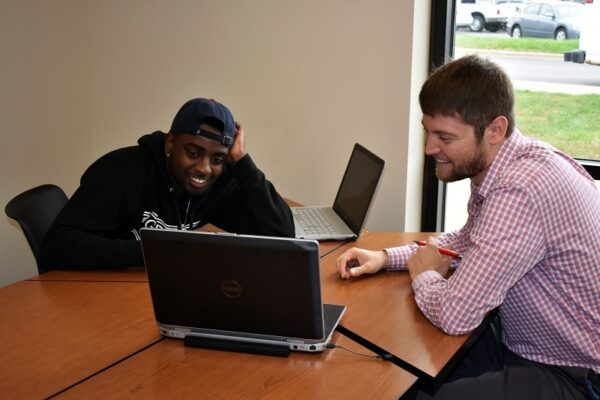 student and instructor sitting at a table with laptops laughing