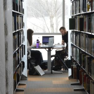 Two students sitting at a desk in front of a window at the library