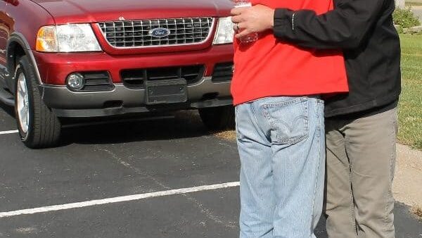 man in red jacket hugging man in black jacket in parking lot front of red Ford Explorer