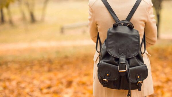 female student with back to camera wearing backpack in autumn park