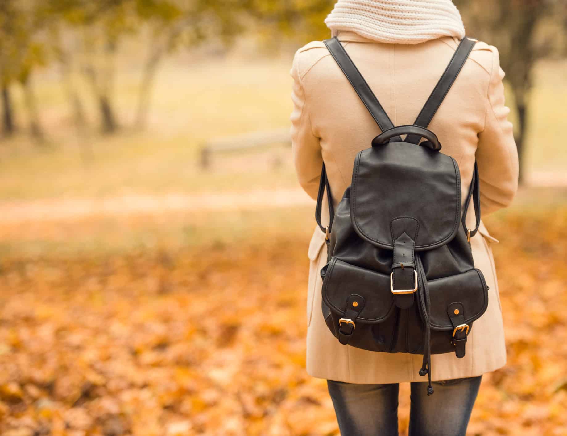 female student with back to camera wearing backpack in autumn park