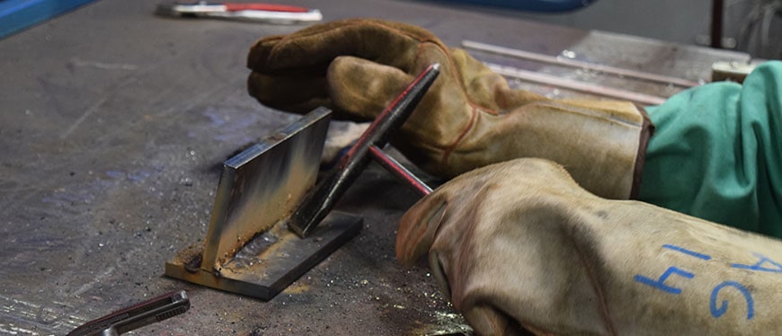 Hands in welding cloves working with metal tools