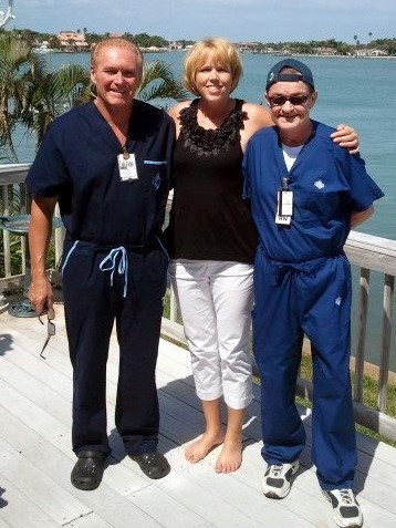 woman with arms around 2 men in scrubs standing on sunny balcony